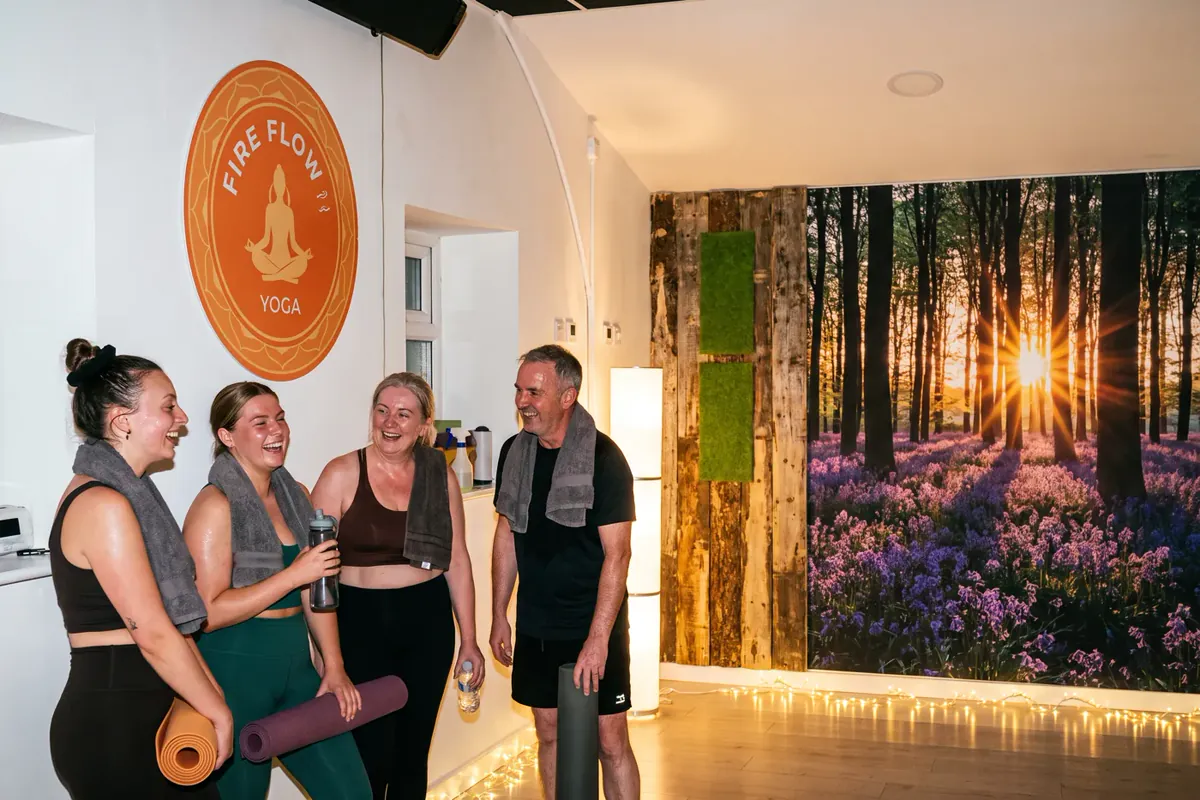 Four people with mats in the heated studio in front of the bluebell forest mural