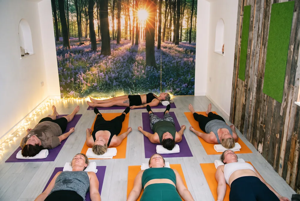 The Fire Flow studio at the end of class: students lying on orange and purple mats under the bluebell forest mural