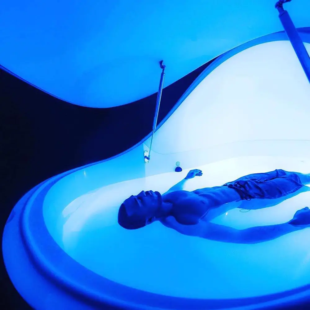 A man floating on his back in a pod lit blue.